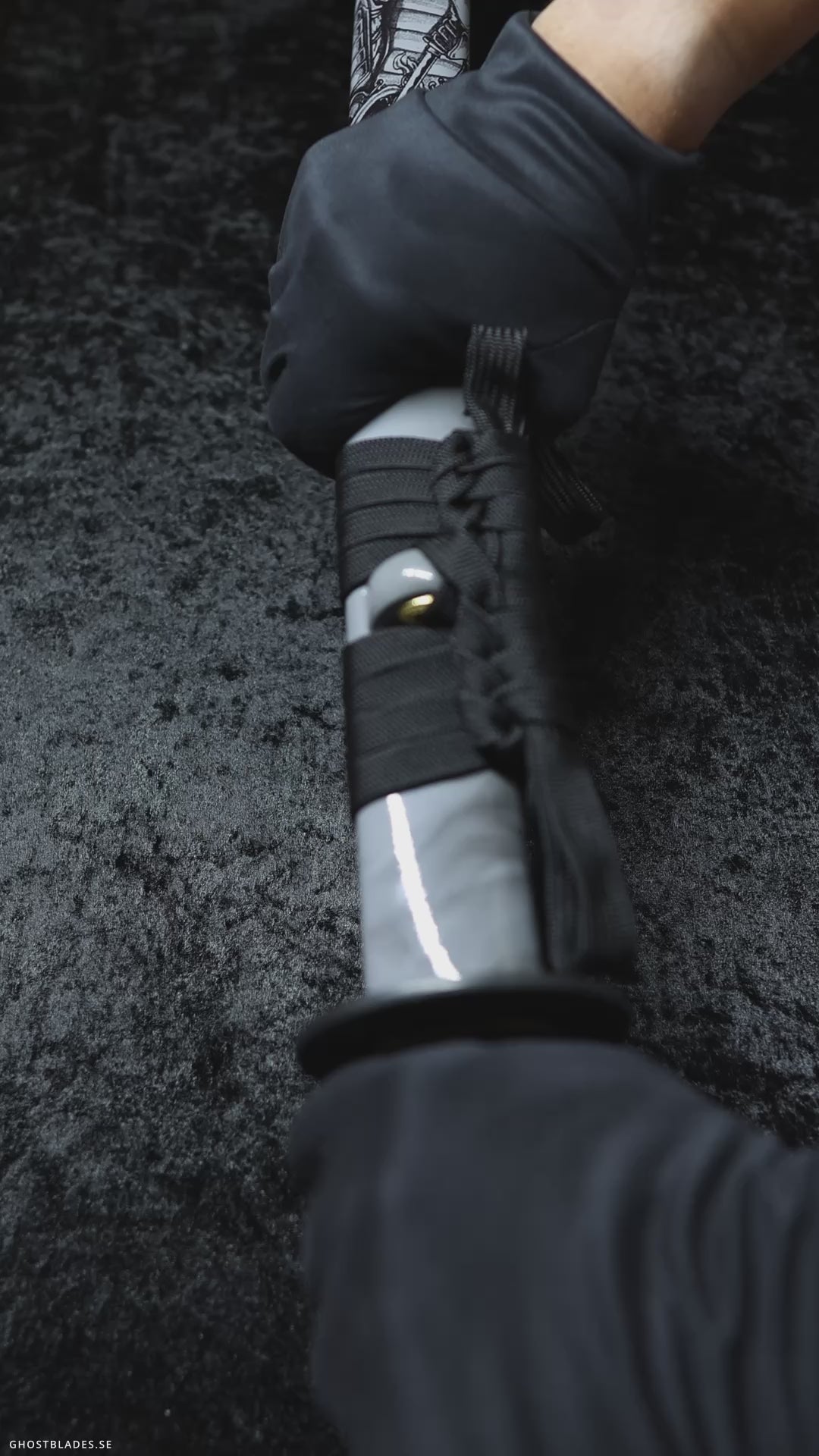 Cinematic showcase of the Tenebris Creed Katana by Ghost Blades - handmade samurai sword in T10 steel with genuine hamon, white saya with black art motifs and gold-detailed fittings symbolizing loyalty and darkness.